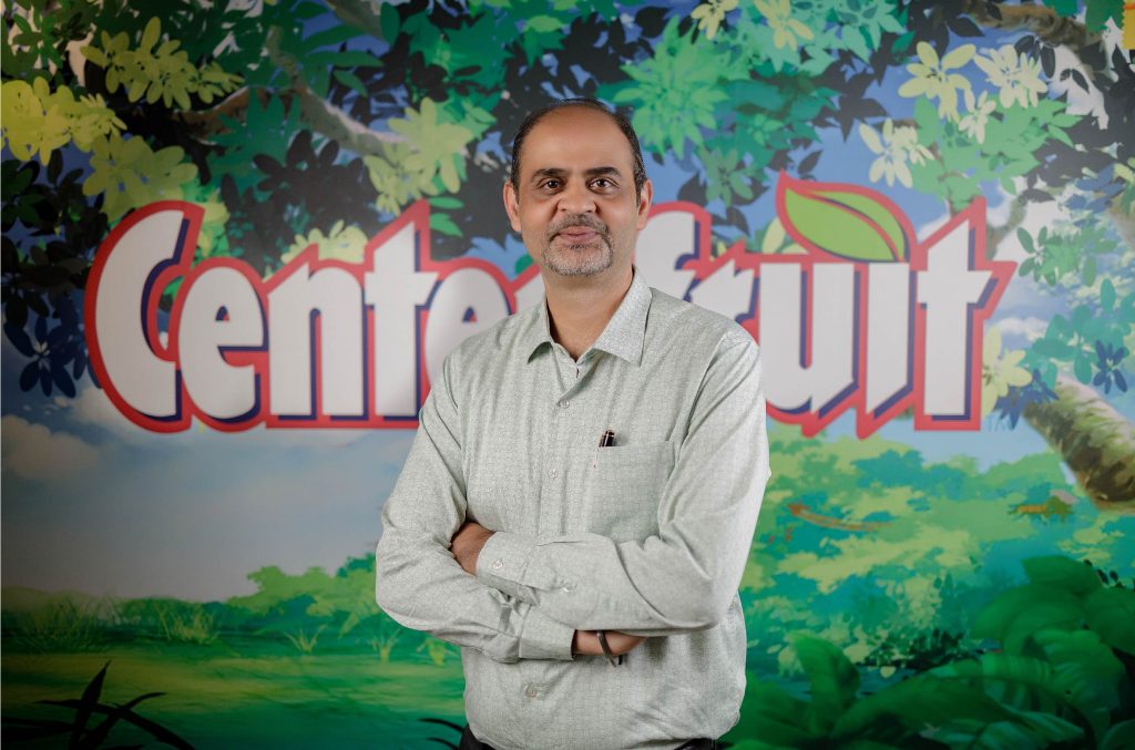 Ashish Kapoor, Managing Director of Perfetti Van Melle (PVM) Bangladesh standing in front of a Centerfruit poster