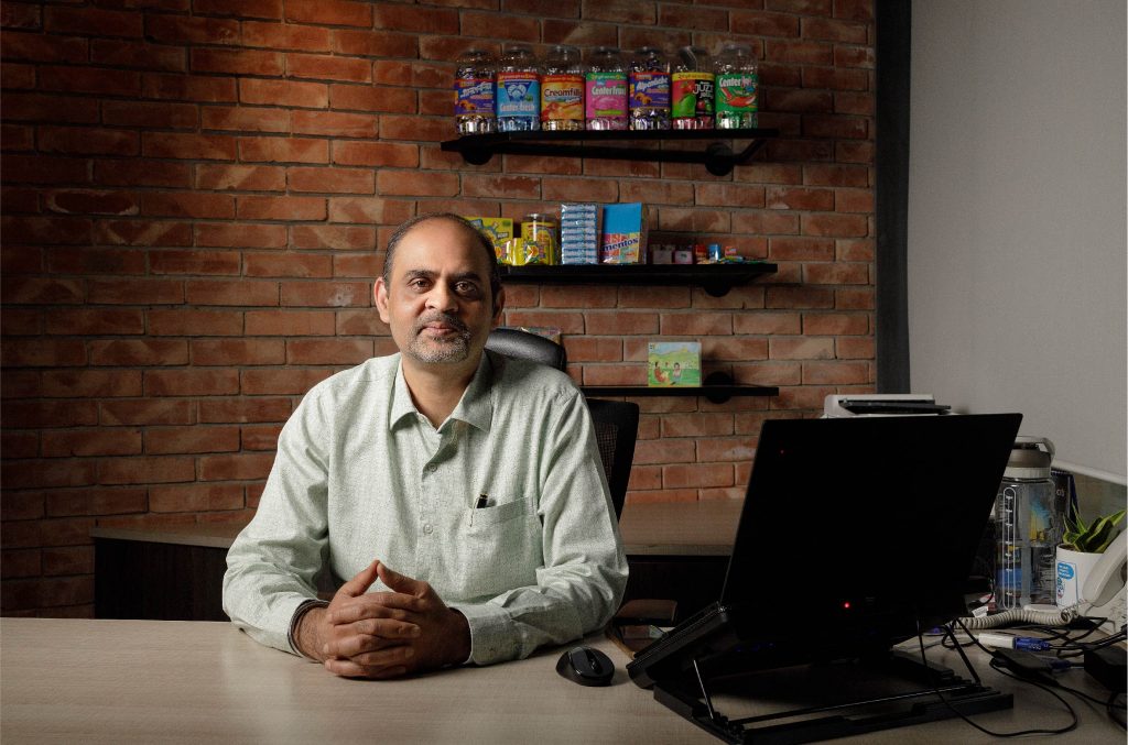 Ashish Kapoor Managing Director of Perfetti Van Melle (PVM) Bangladesh sitting at his desk in front of confectionery products made by PVM Bangladesh